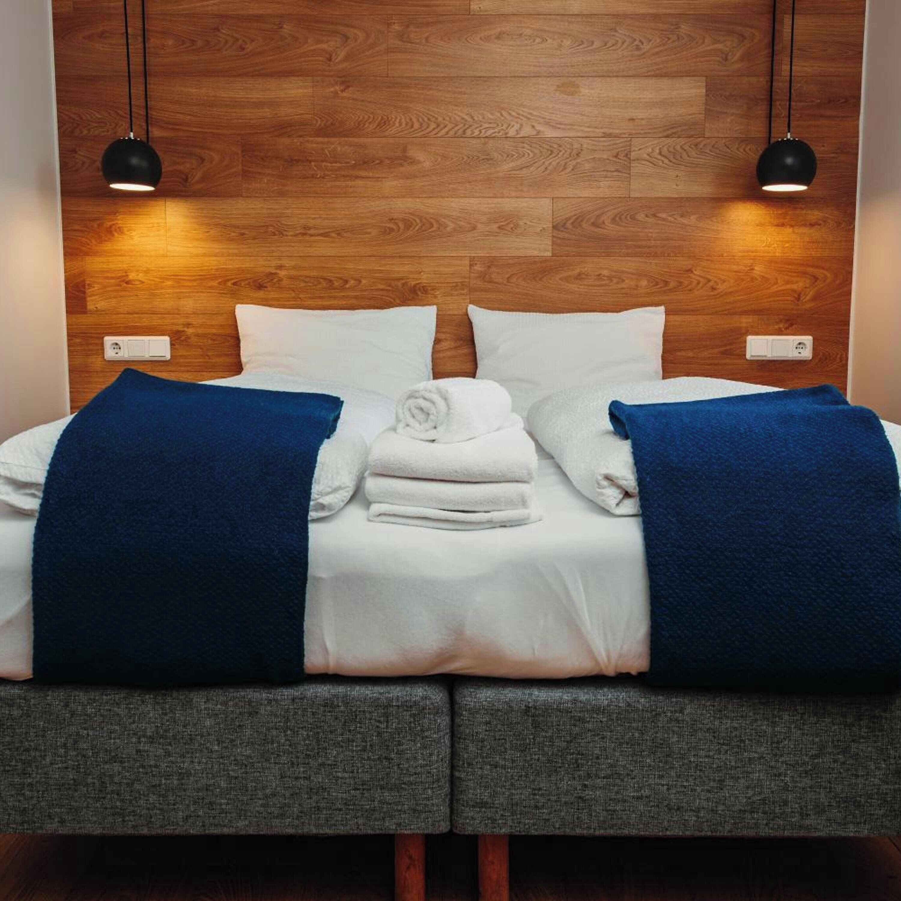 A neatly made bed with white linens, two blue throw blankets, and folded towels.