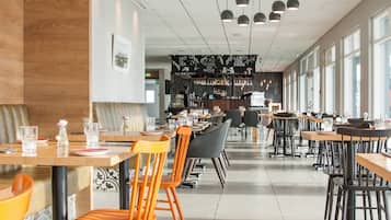 A modern restaurant with wooden flooring, black and orange chairs, and a bar area with a black and white theme.