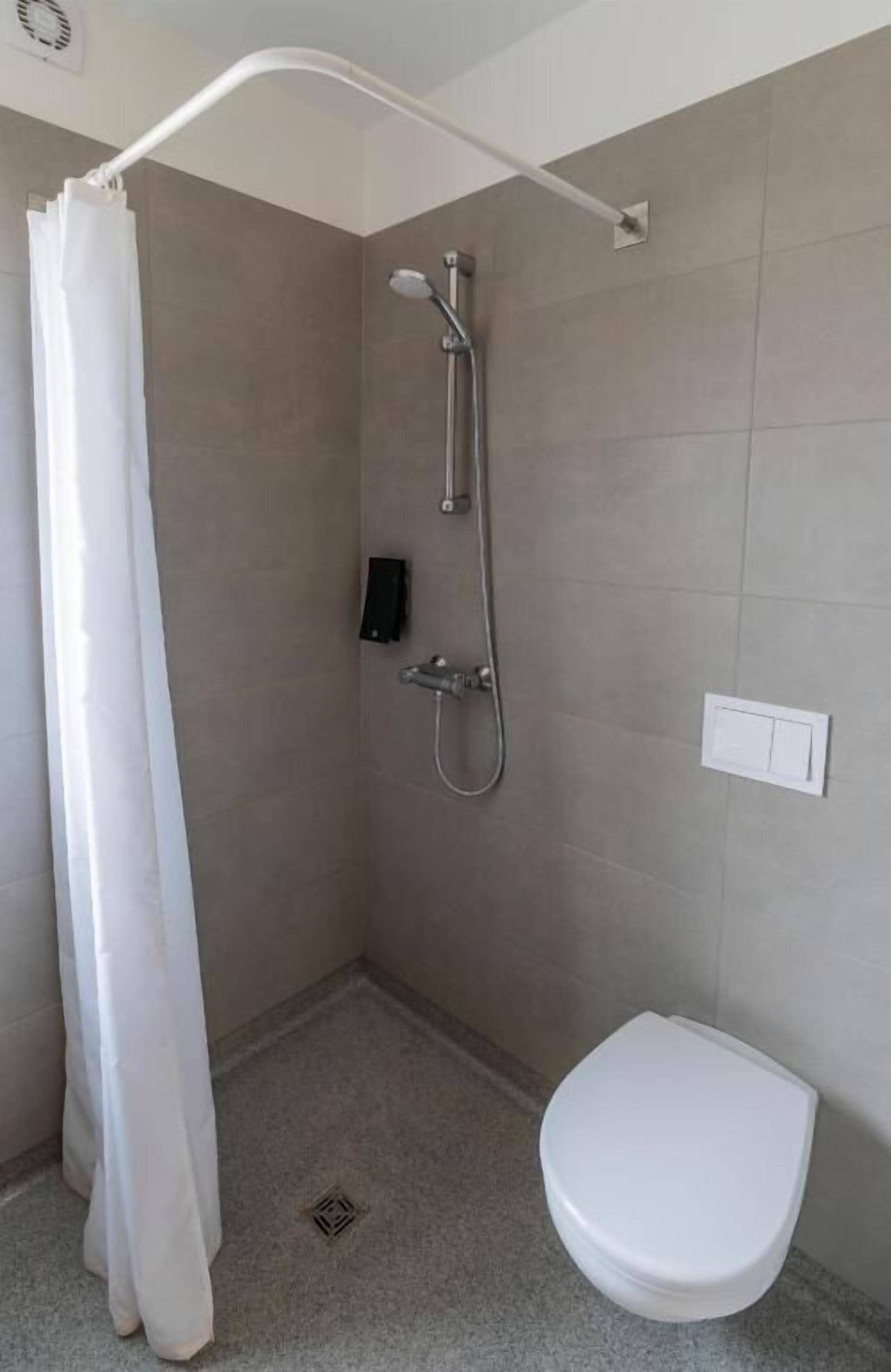 A bathroom with a shower, toilet, and a wall-mounted control panel.