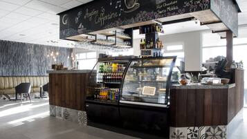 A coffee shop interior with a chalkboard menu, seating area, and a display case with beverages.