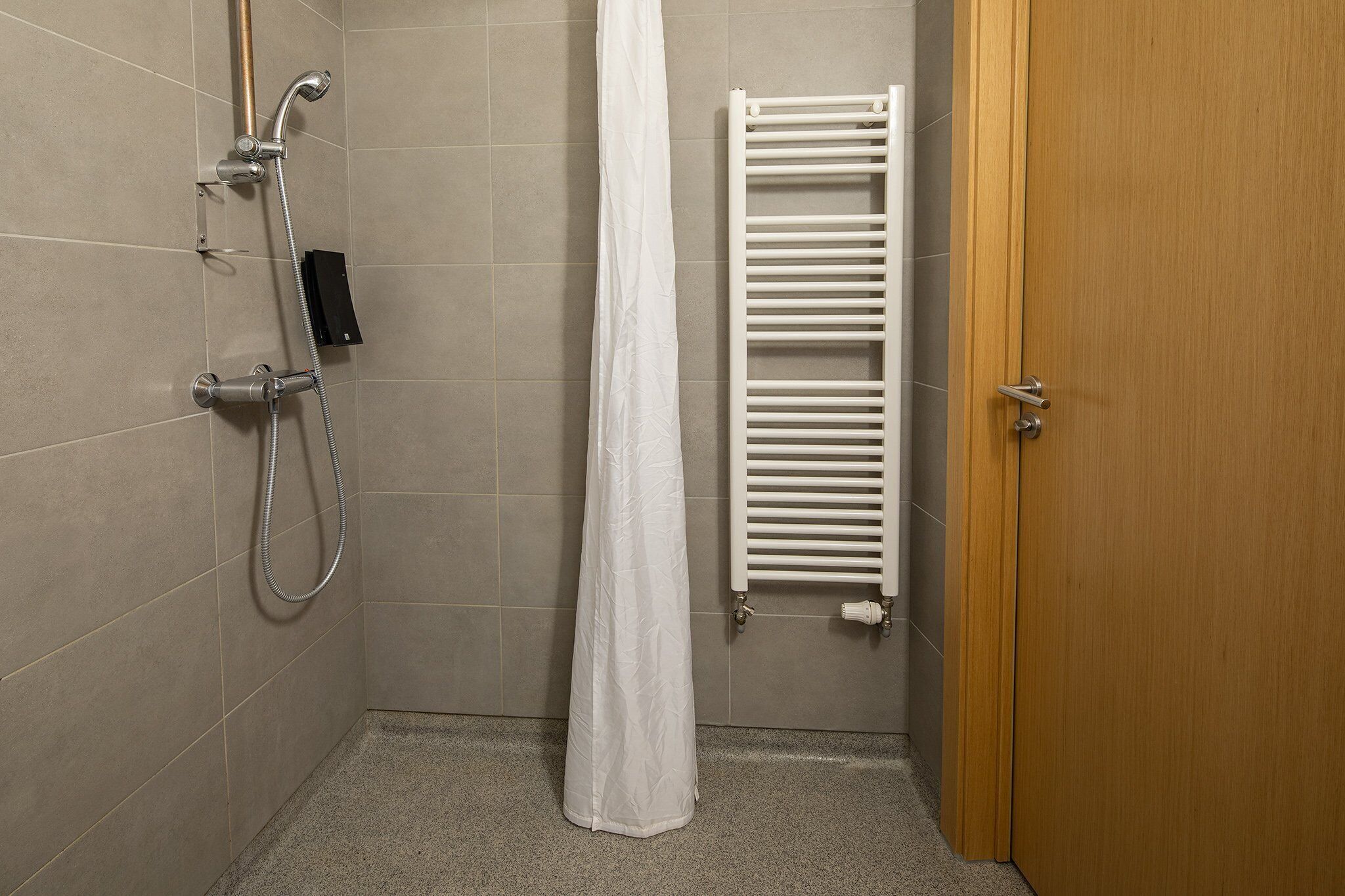 Un espacio para ducha con cortina blanca, un cabezal de ducha de mano y un perchero en la pared.
