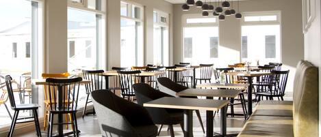 A spacious dining area with multiple tables and chairs, large windows, and hanging pendant lights.