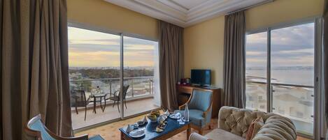 Quarto de hotel com varanda, sofá, mesa de jantar com louça e televisão.