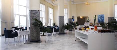 A spacious hotel lobby with high ceilings, large windows, and a central island with a buffet.