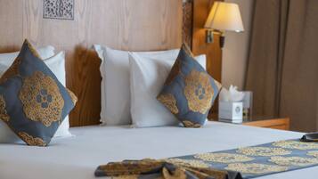 A neatly made bed with a blue and gold patterned pillow, a white pillow, and a folded blanket with a similar pattern.