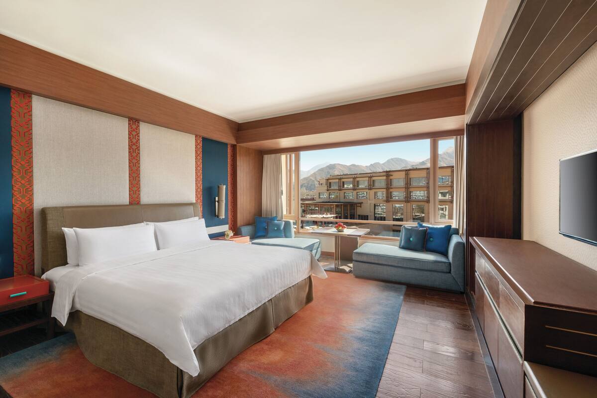 Una habitación de hotel con una cama grande, un sofá, un televisor y vistas a las montañas.