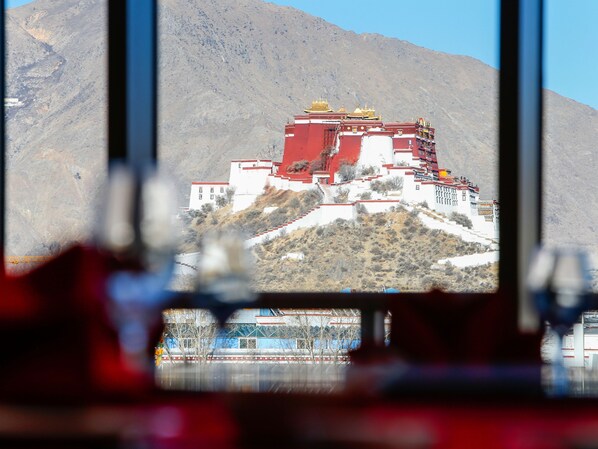 A large, red and white building with golden roofs, situated on a hill with a mountainous backdrop. - Shangri-La Lhasa (Lhasa)