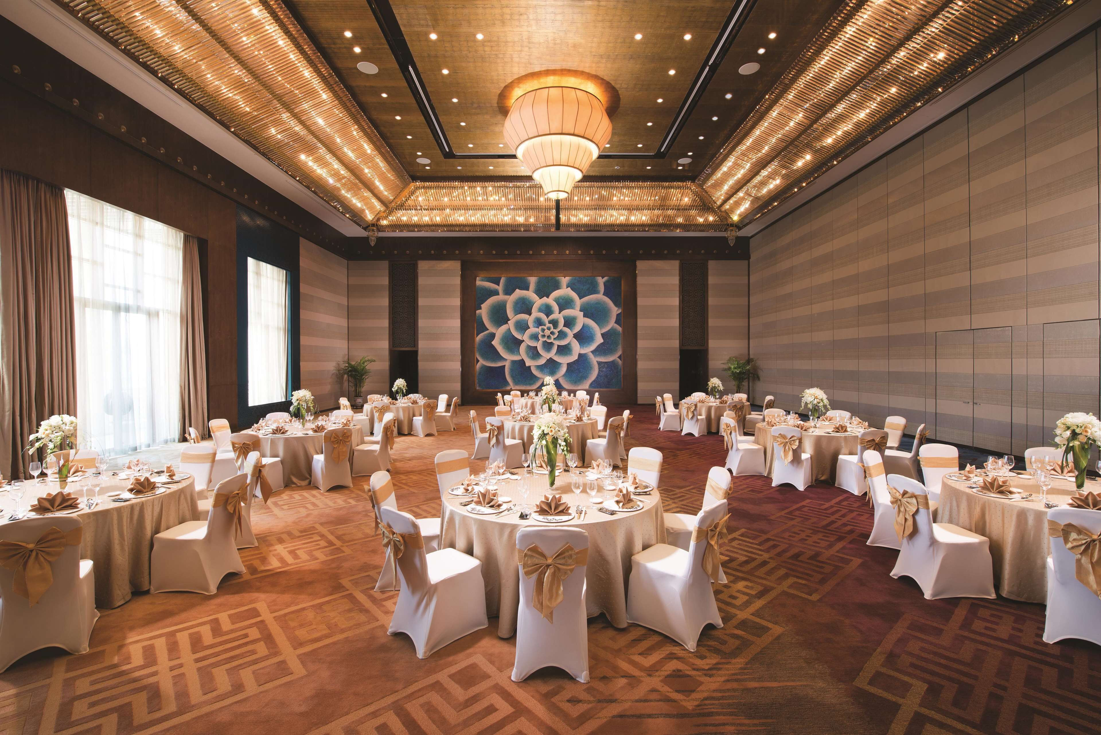 A banquet hall with round tables set for a formal event, featuring white tablecloths and gold sashes.