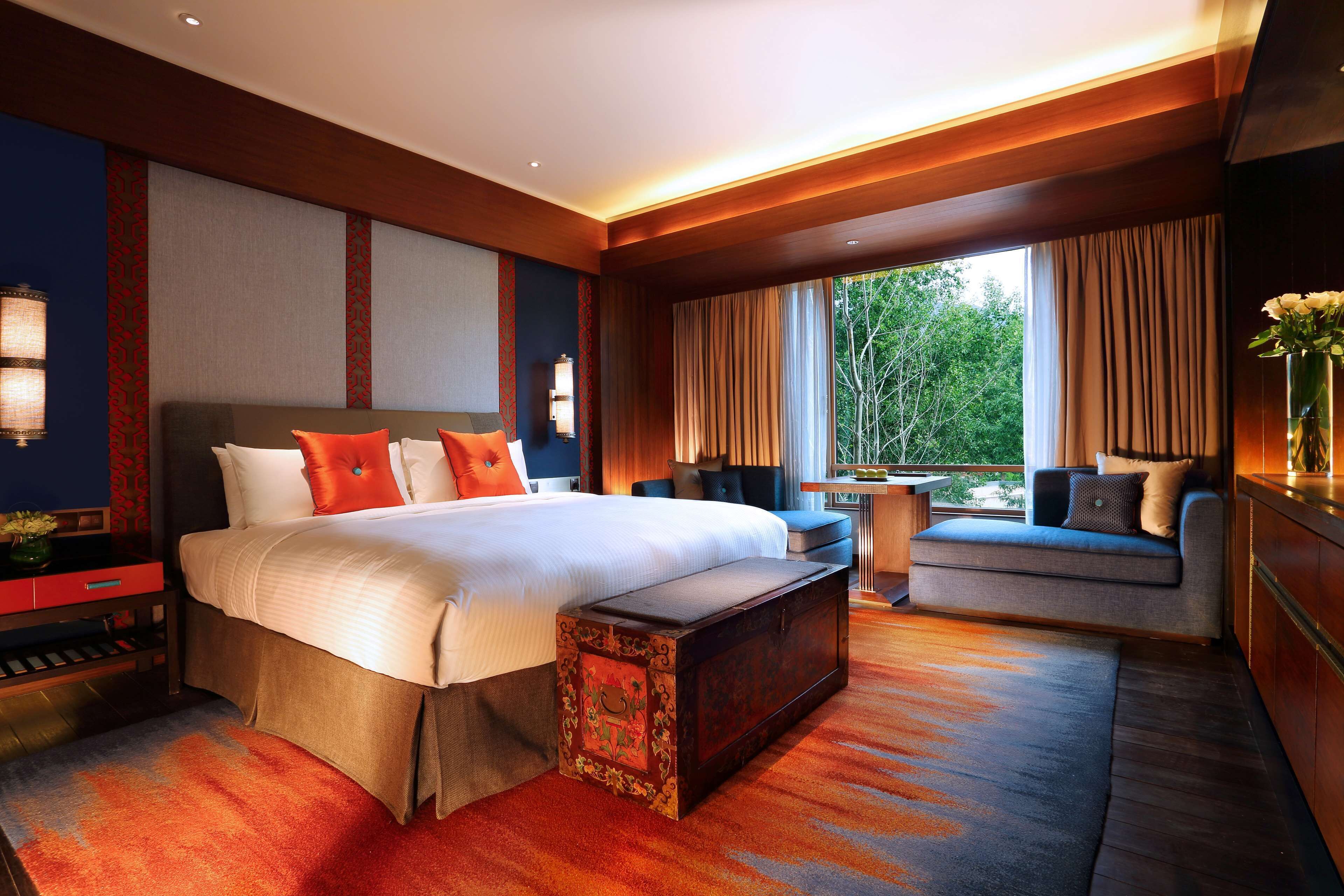 A modern hotel room with a large bed, a sofa, a small table, and a view of the outdoors.