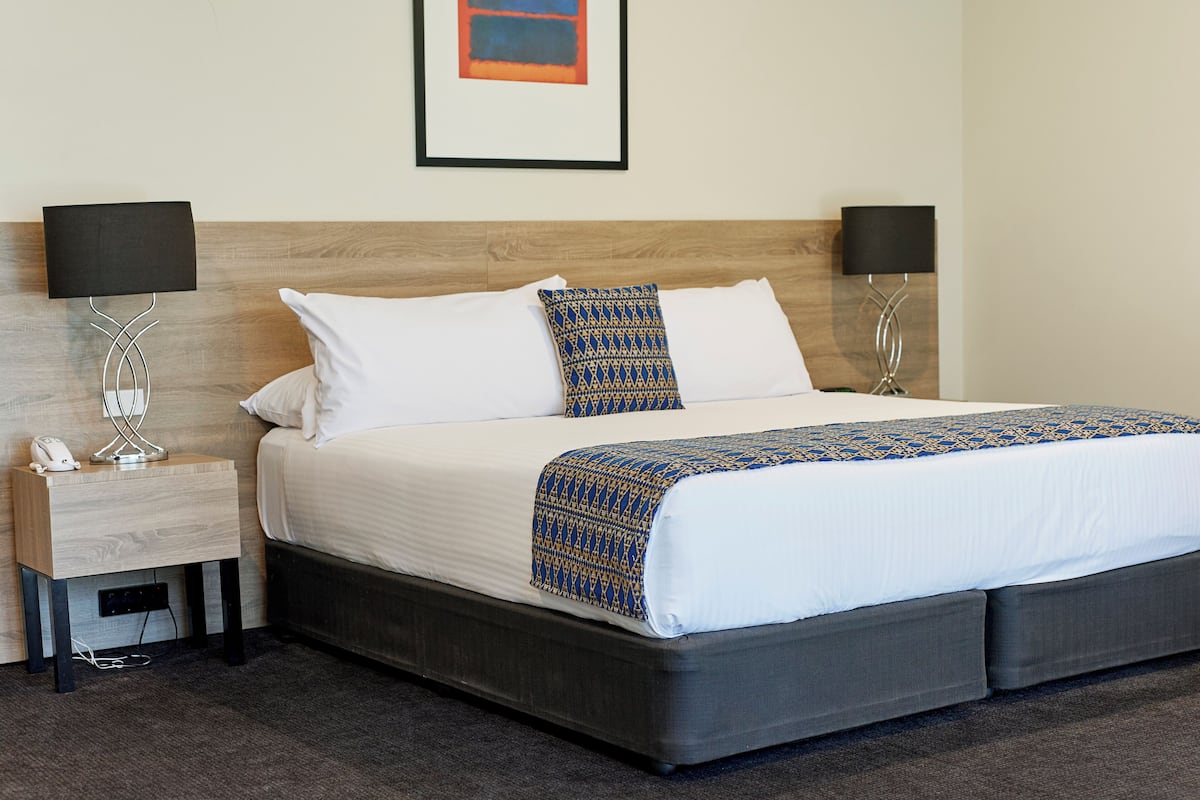 A neatly made bed with a patterned blanket, two bedside lamps, a nightstand with a phone, and a framed picture on the wall.