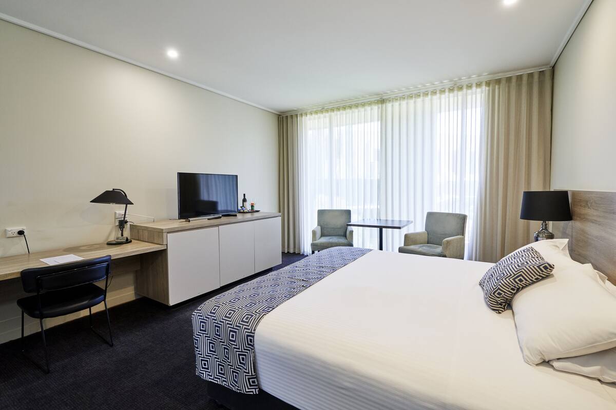 A hotel room with a large bed, a desk with a computer, a TV, and two chairs.