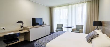 Habitación de hotel con una cama grande, un escritorio con computadora, un televisor y dos sillas.
