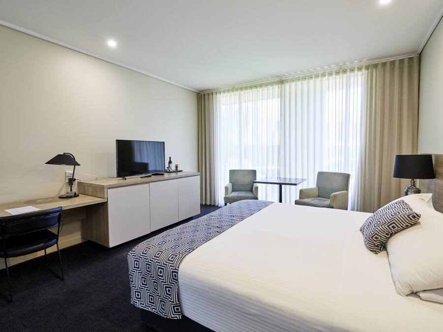 Une chambre d’hôtel avec un grand lit, un bureau avec un ordinateur, une télévision et deux chaises.