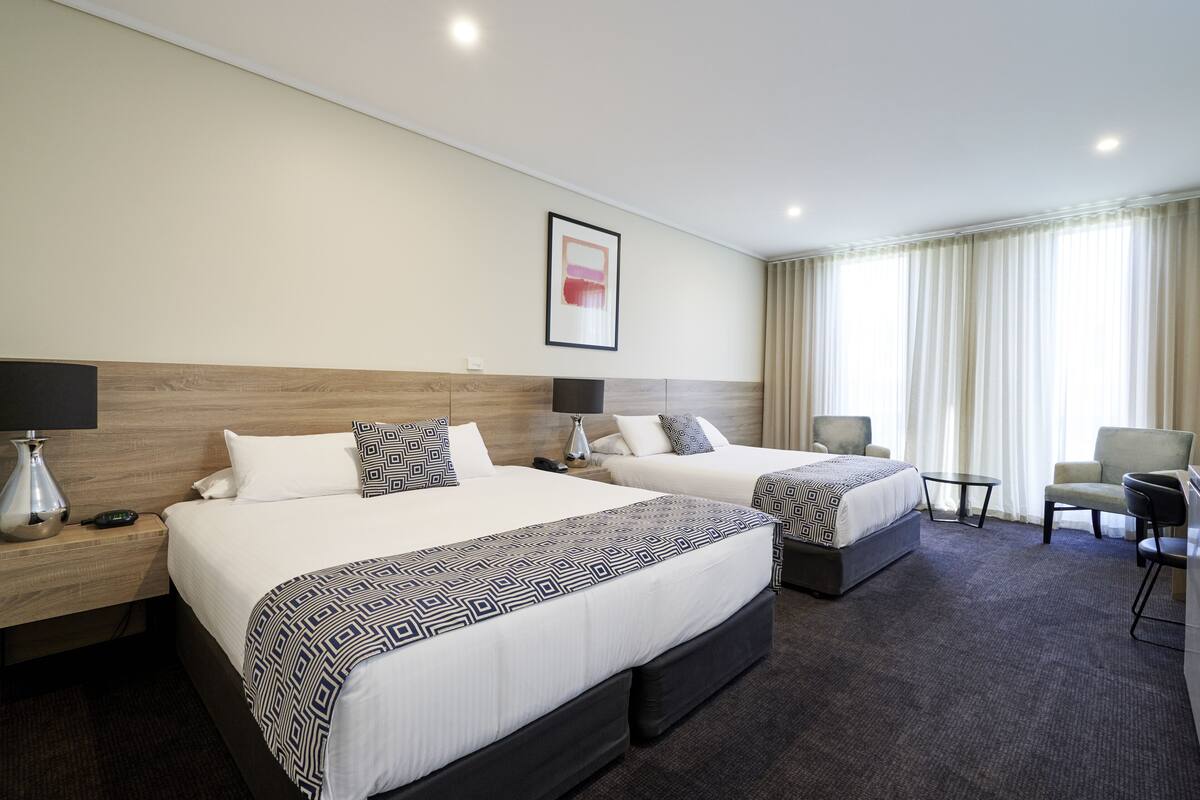 A hotel room with two beds, a desk, a chair, and a large window with curtains.