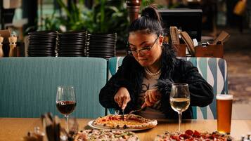 Una persona seduta a un tavolo con diverse pizze e bevande.