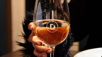 A glass of wine on a wooden table with a plate of food in the background.