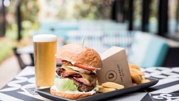 Una bandeja con una hamburguesa, papas fritas y una cerveza, con una piscina al fondo.