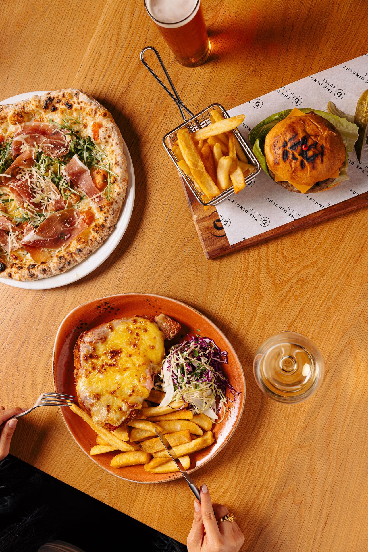 Una mesa con una pizza, una hamburguesa, papas fritas y una cerveza en un vaso.