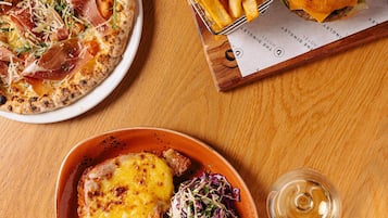 Una mesa con una pizza, una hamburguesa, papas fritas y una cerveza en un vaso.