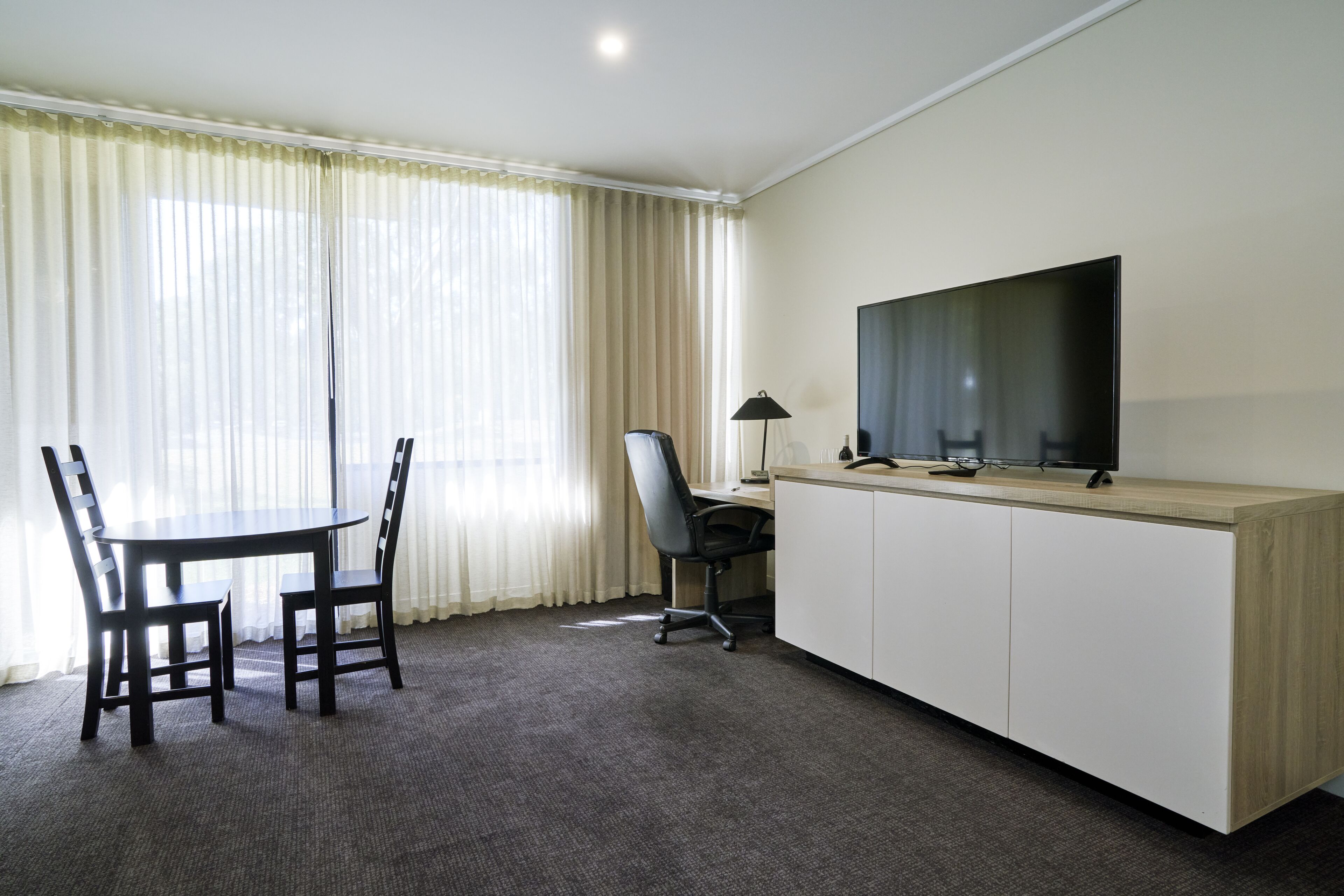 A hotel room with a wooden desk, a television, a chair, and a lamp.