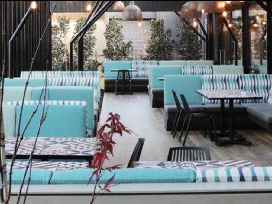 Un área de estar exterior moderna con sofás azul claro y mesas, rodeada de listones verticales de madera.