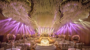 Un espacio para eventos formales con mesas redondas, sillas blancas y centros de mesa florales.