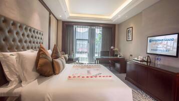 A hotel room with a large bed, a TV on the wall, and a view of the outdoors through the window.