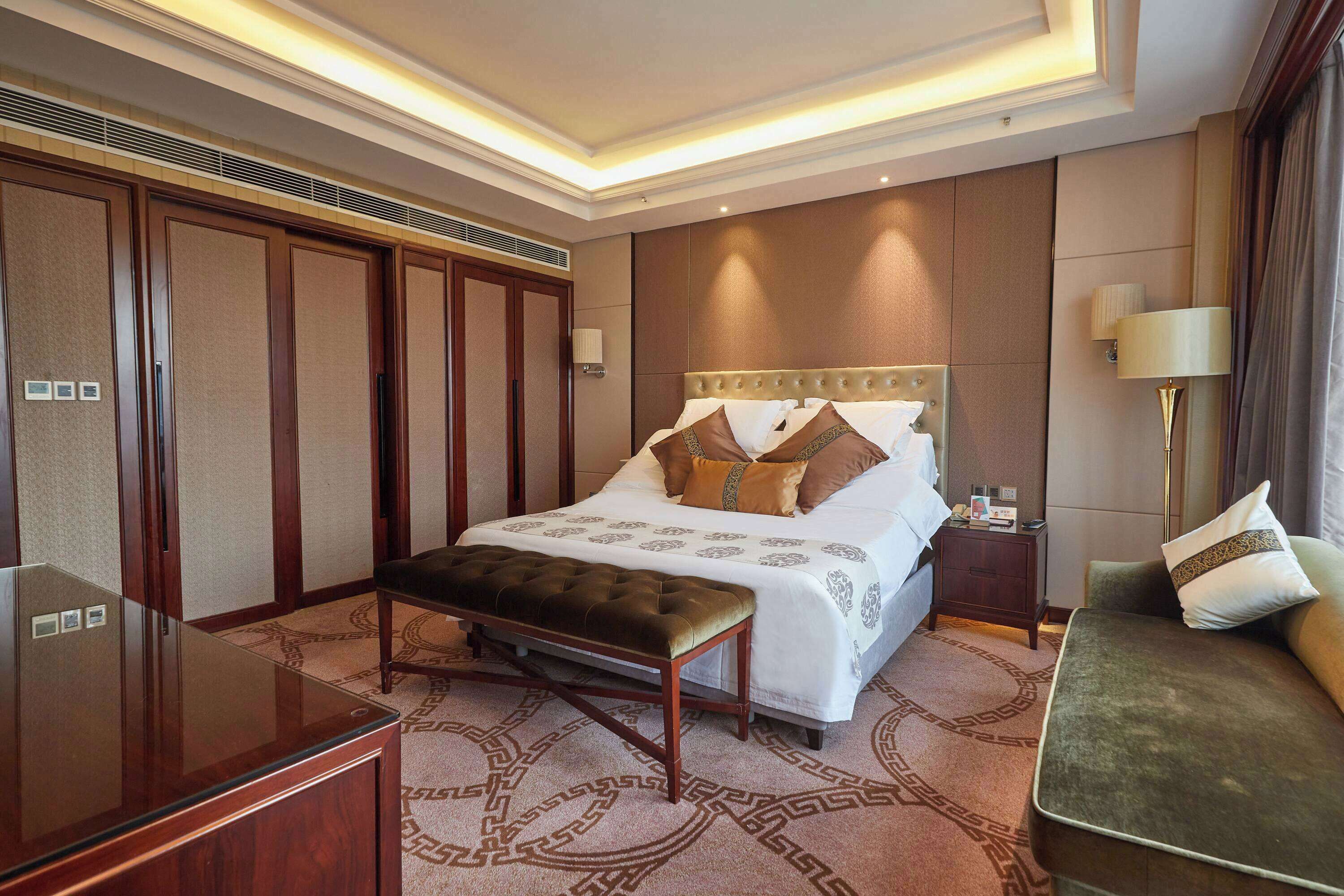 A hotel room with a large bed, a bench, a desk, and a sofa.