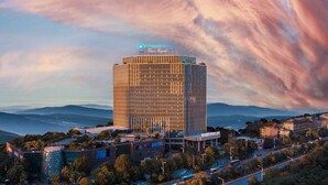 Un hotel de gran altura con fachada de vidrio moderna, rodeado de un exuberante paisaje verde y montañas al fondo.