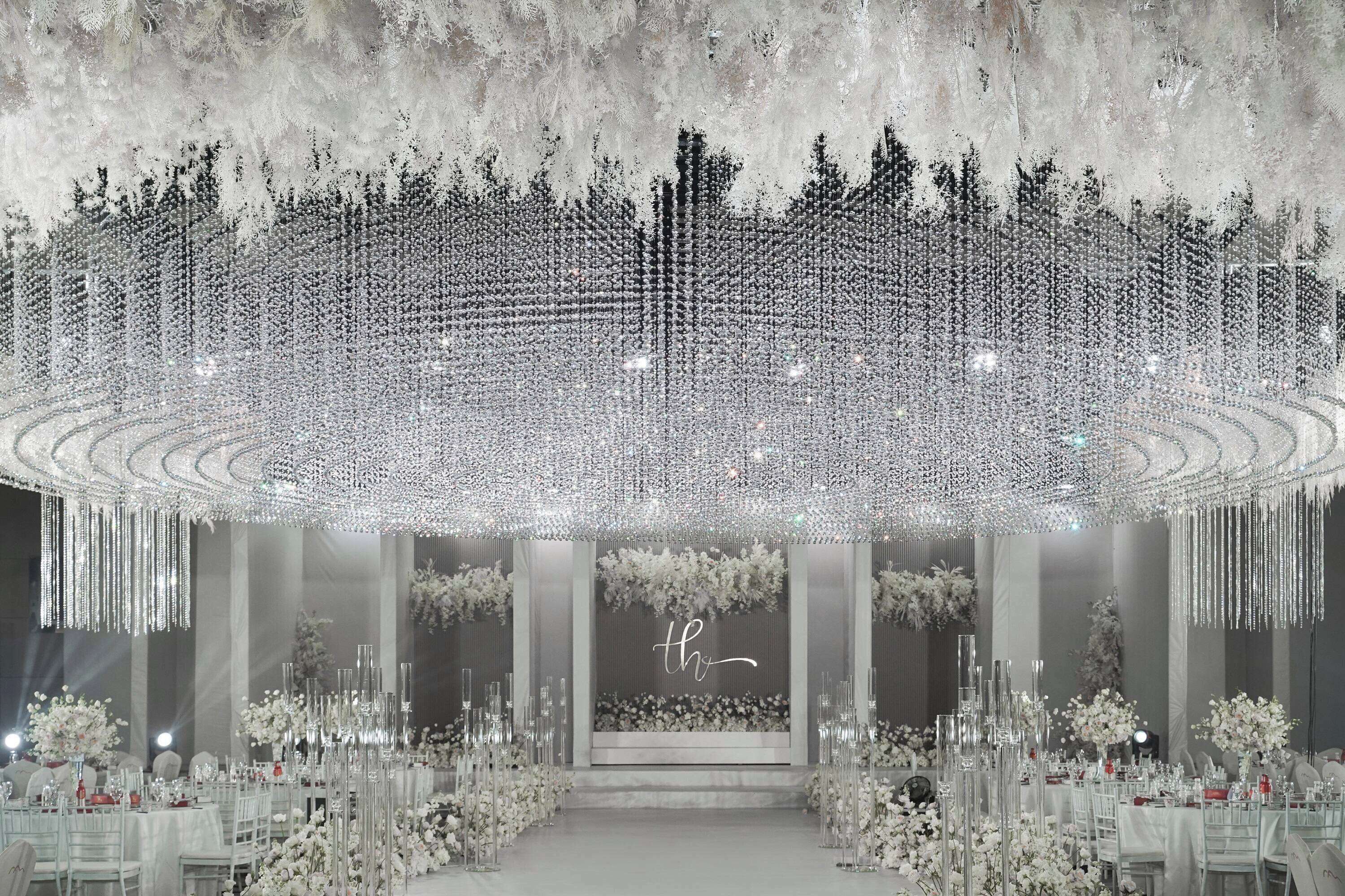 Un salón imponente con un escenario central, rodeado de filas de mesas y sillas, decorado con arreglos florales y altos candelabros de cristal.