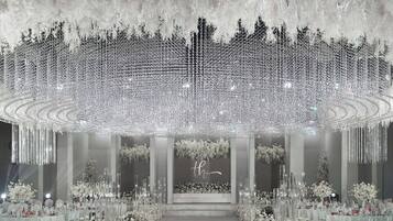 Un salón imponente con un escenario central, rodeado de filas de mesas y sillas, decorado con arreglos florales y altos candelabros de cristal.