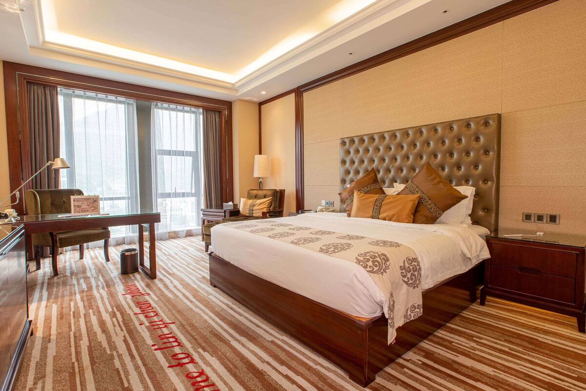A hotel room with a large bed, a desk, a chair, a lamp, and a window with curtains.