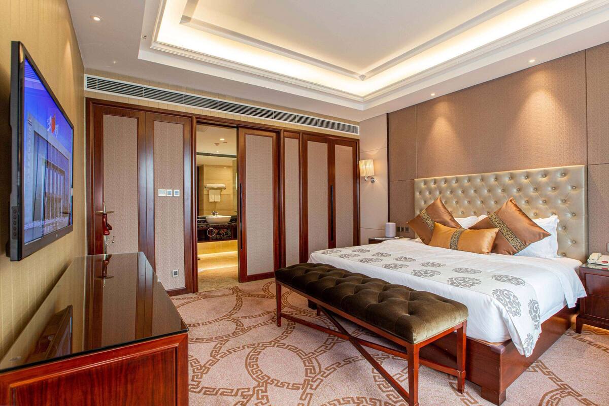 A hotel room with a large bed, a bench, a TV, and a walk-in closet.