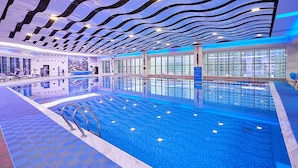Una amplia piscina interior con un diseño moderno en el techo, ventanas claras y suelo de baldosas.