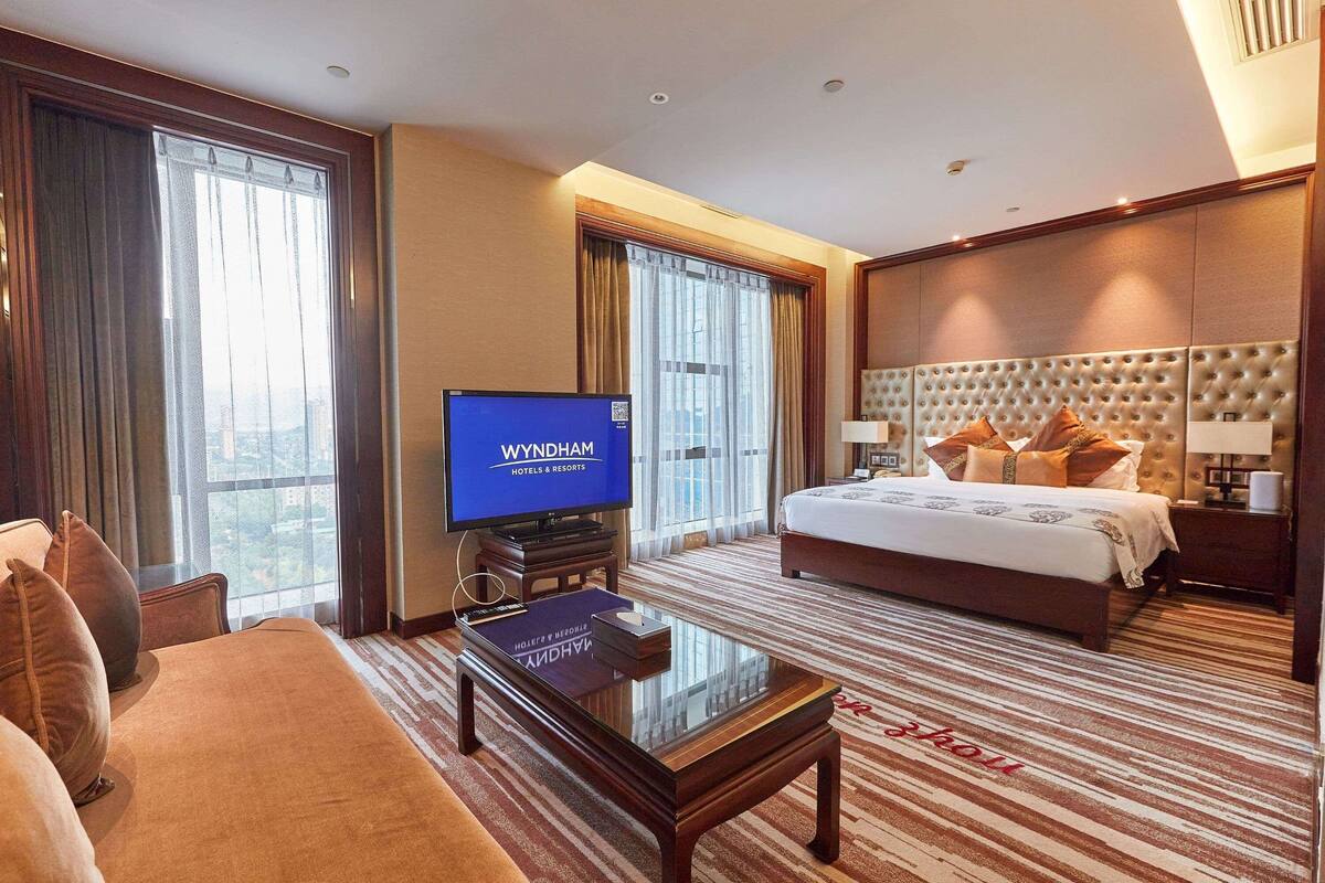 A hotel room with a large bed, a television, a coffee table, and a sofa.