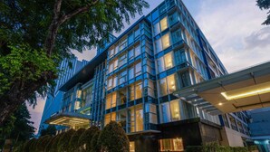 A modern building with a glass facade, a covered entrance, and a landscaped area with trees. - Mercure Jakarta Sabang (Jakarta)