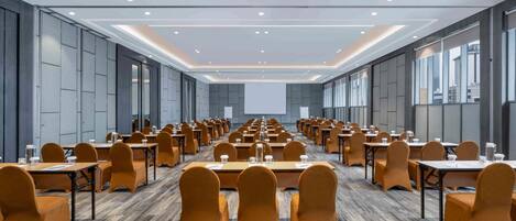 Un salón de conferencias con filas de mesas y sillas, una pantalla grande al frente y un diseño moderno en el techo.