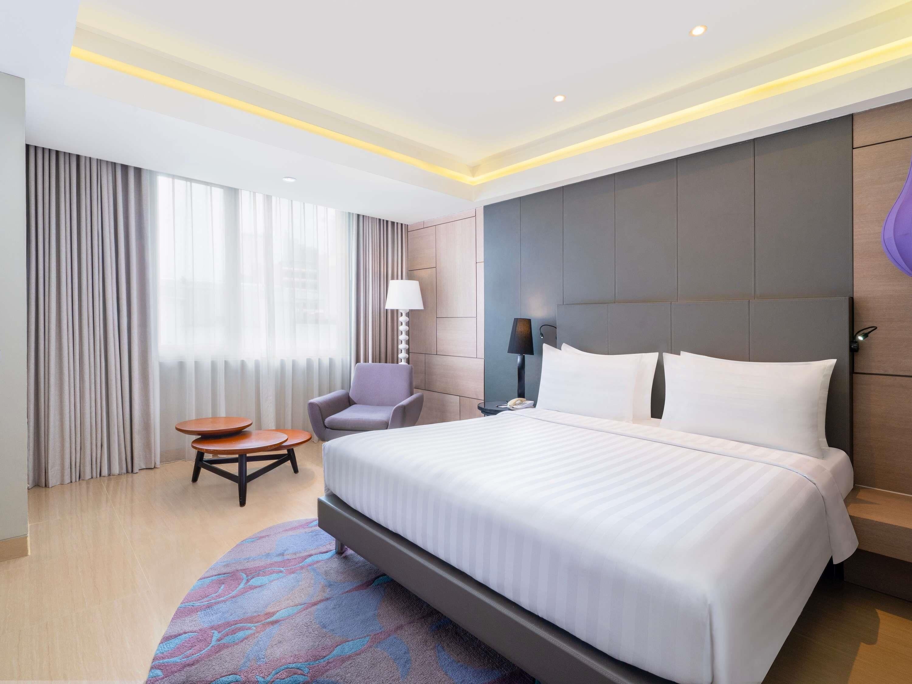 A hotel room with a large bed, a chair, a small table, and a lamp.