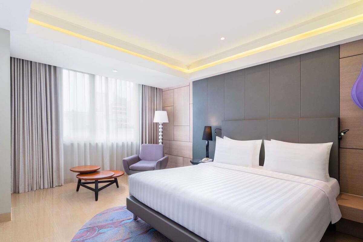 A hotel room with a large bed, a chair, a small table, and a lamp.