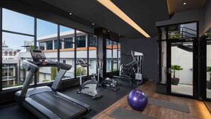 A modern gym with a treadmill, elliptical, and exercise ball, large windows, and a view of buildings. - Mercure Jakarta Sabang (Jakarta)
