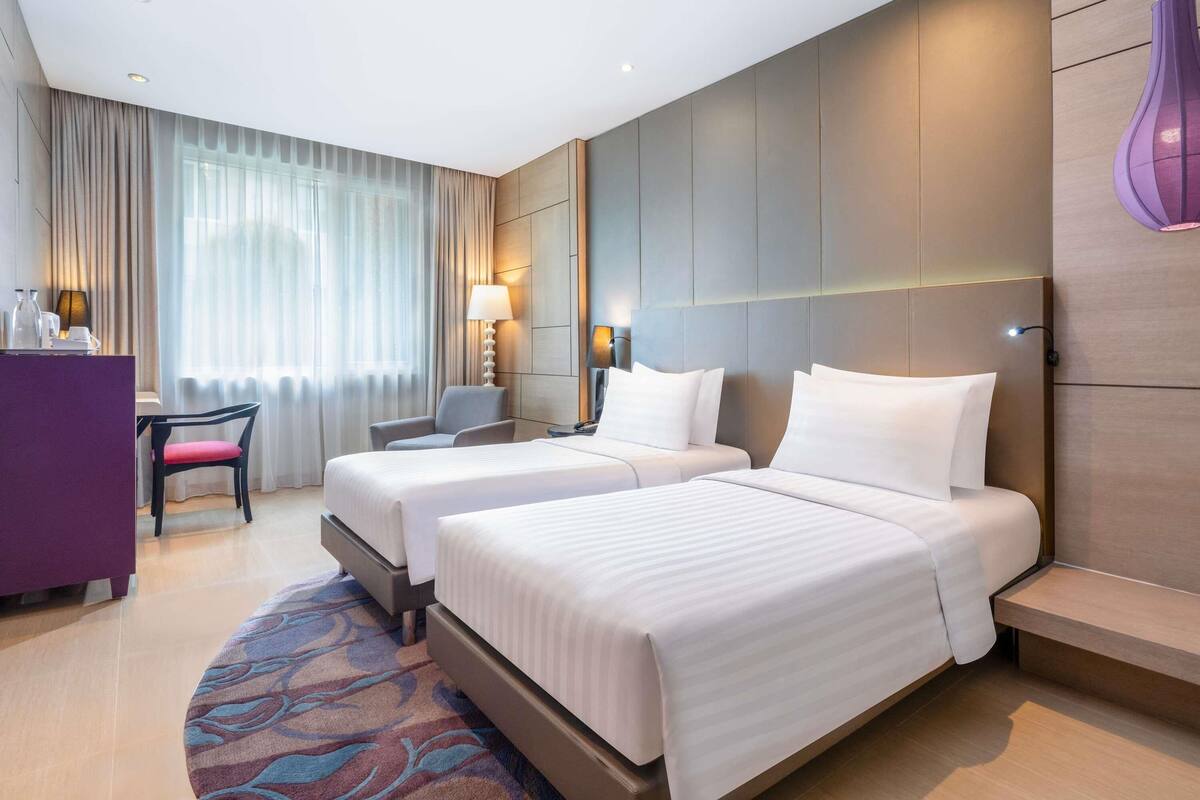 A hotel room with two beds, a desk, a chair, and a large window with curtains.