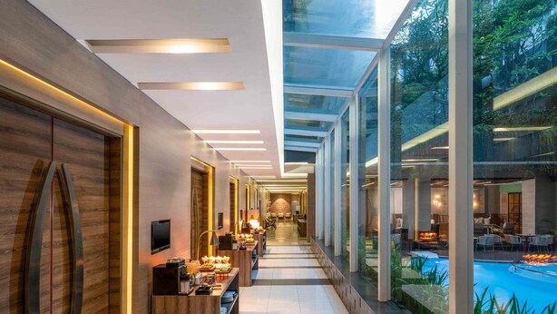 A modern hotel corridor with a glass-enclosed pool area, a reception desk, and a seating area with a view of the pool. - Mercure Jakarta Sabang (Jakarta)