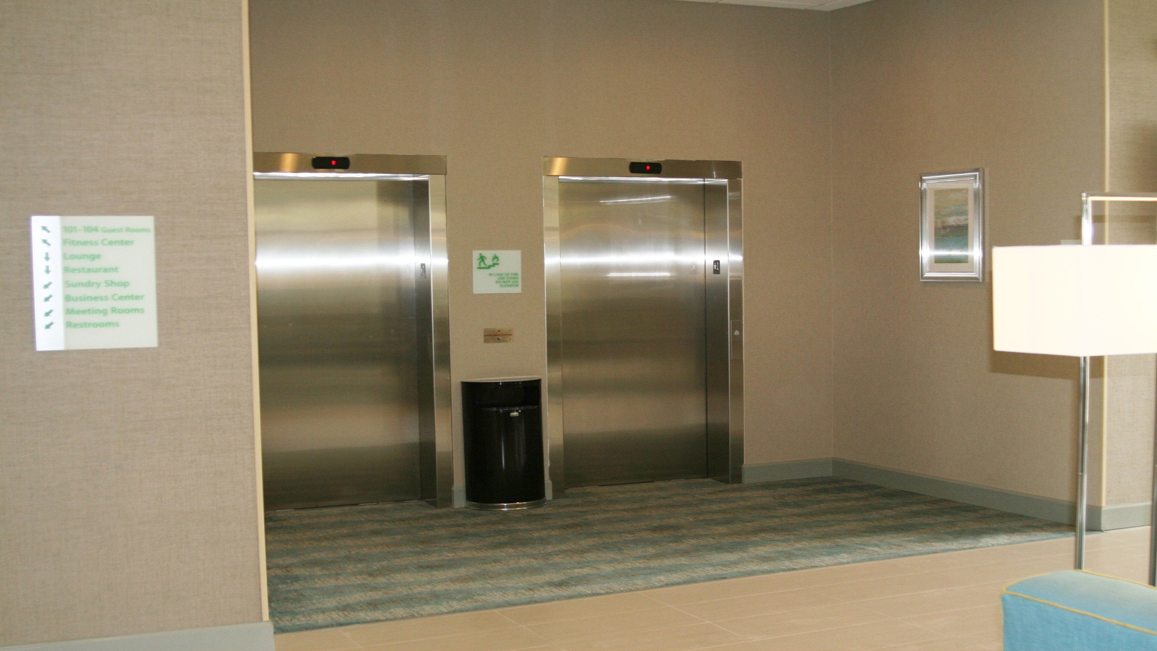 Um elevador de hotel com um painel de parede que lista as comodidades, incluindo centro de fitness, lounge, restaurante, loja de conveniência, centro de negócios, salas de reunião e banheiros.