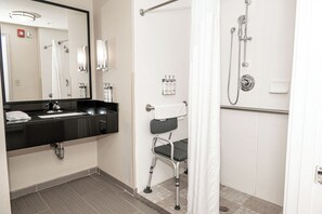 A bathroom with a black sink, a mirror, a shower with a grab bar, and a wheelchair-accessible chair.
