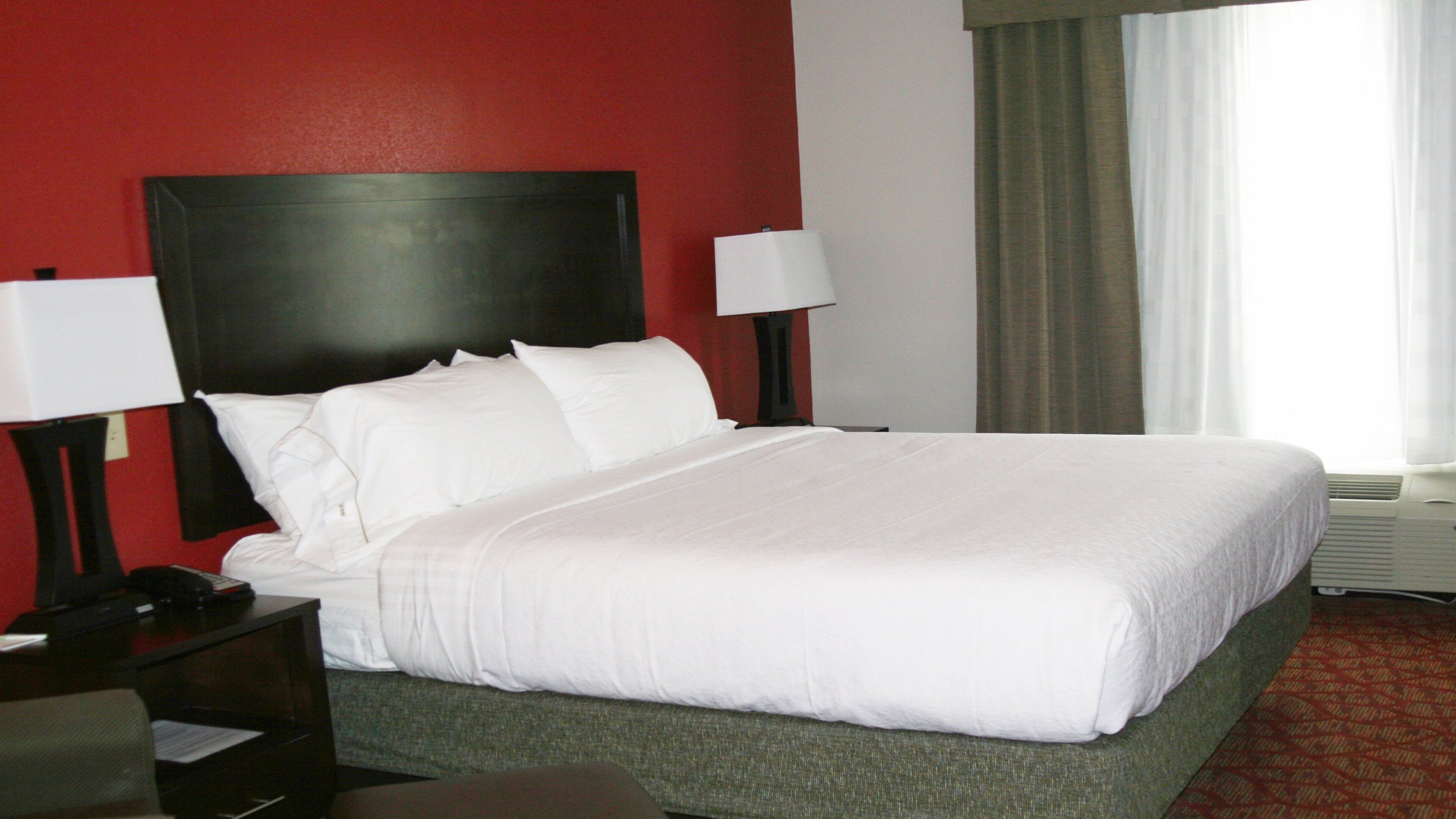 A hotel room with a large bed, two bedside lamps, a nightstand, and a window with curtains.