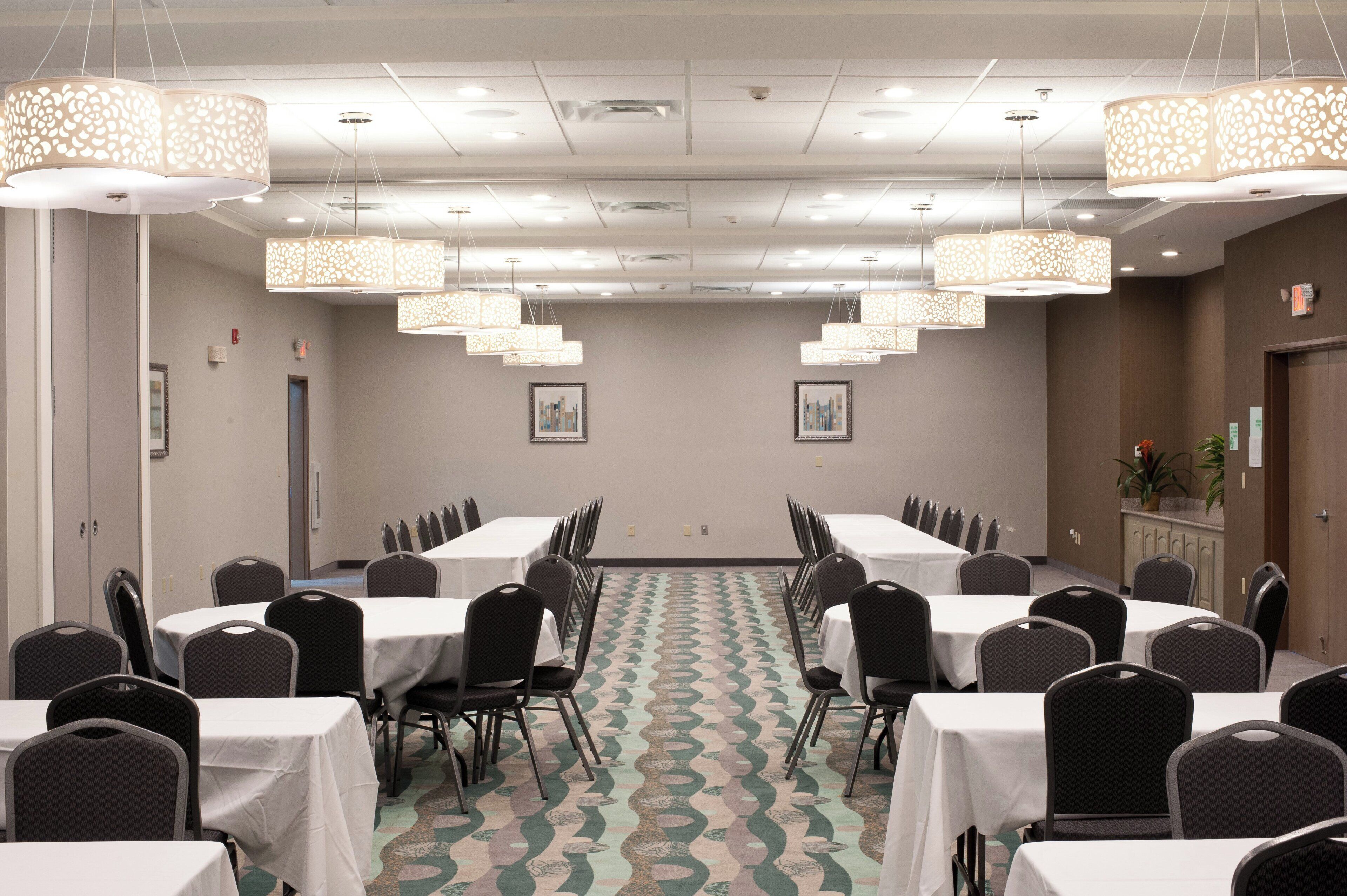 A conference room with tables and chairs, patterned carpet, and hanging light fixtures.