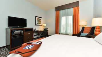 Una habitación de hotel con cama, escritorio con computadora, televisor y ventana con cortinas.