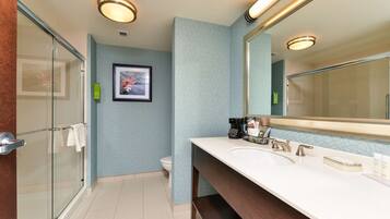 Un baño moderno con ducha de vidrio, lavamanos blanco y un espejo grande, y pared de color azul claro con estampado.