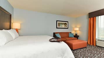 Quarto de hotel com uma cama grande, um sofá, uma mesinha e um quadro na parede.