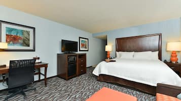 A hotel room with a bed, desk, chair, television, and artwork on the wall.